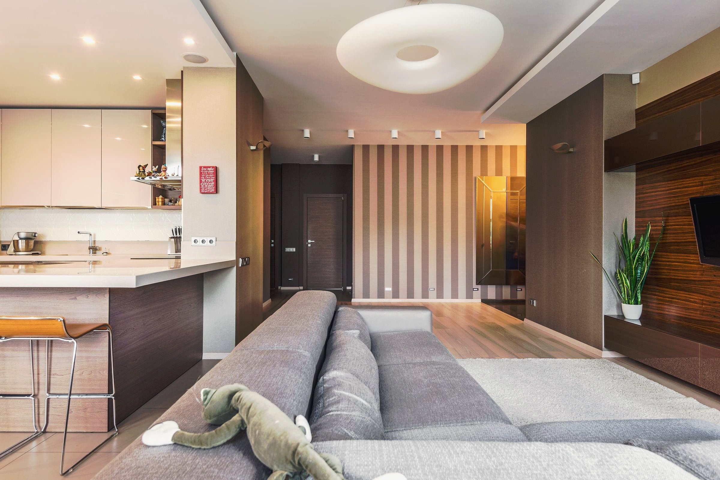A modern open-plan apartment with a grey sofa and a kitchen bar.