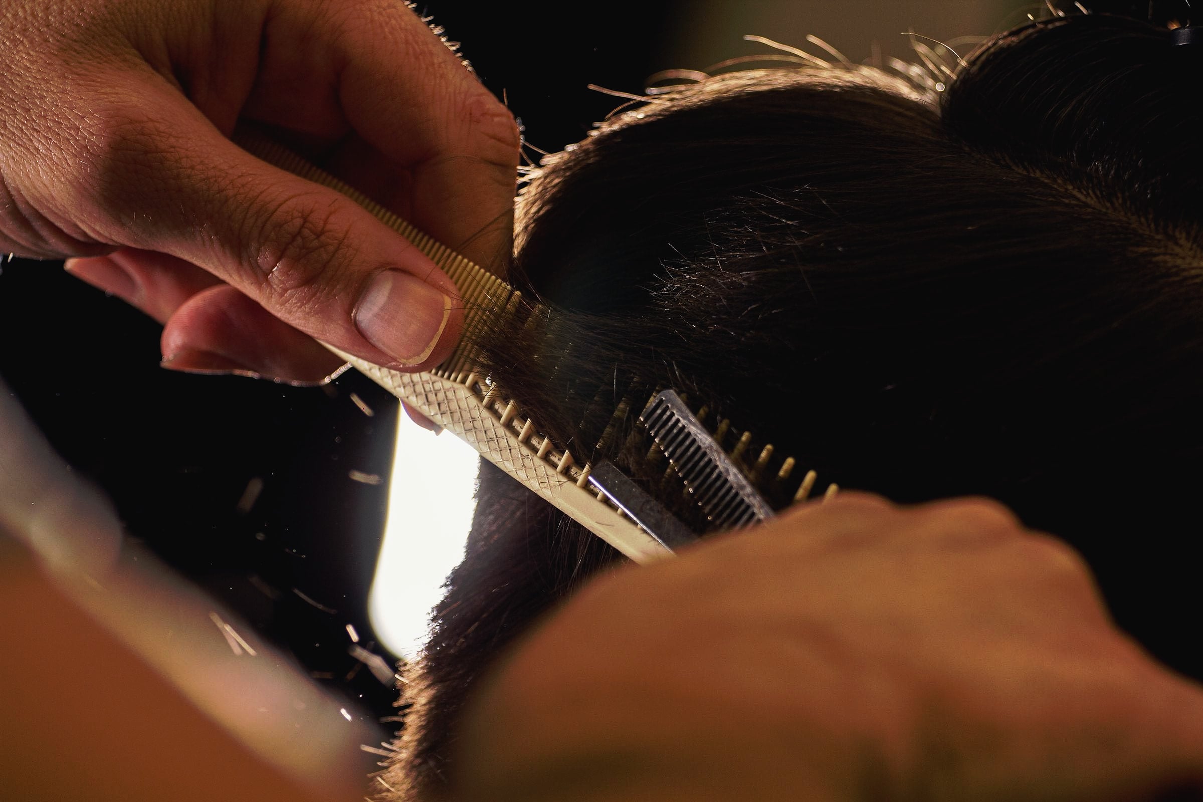 Close-up of a hairdresser's hands cutting hair with comb and scissors.