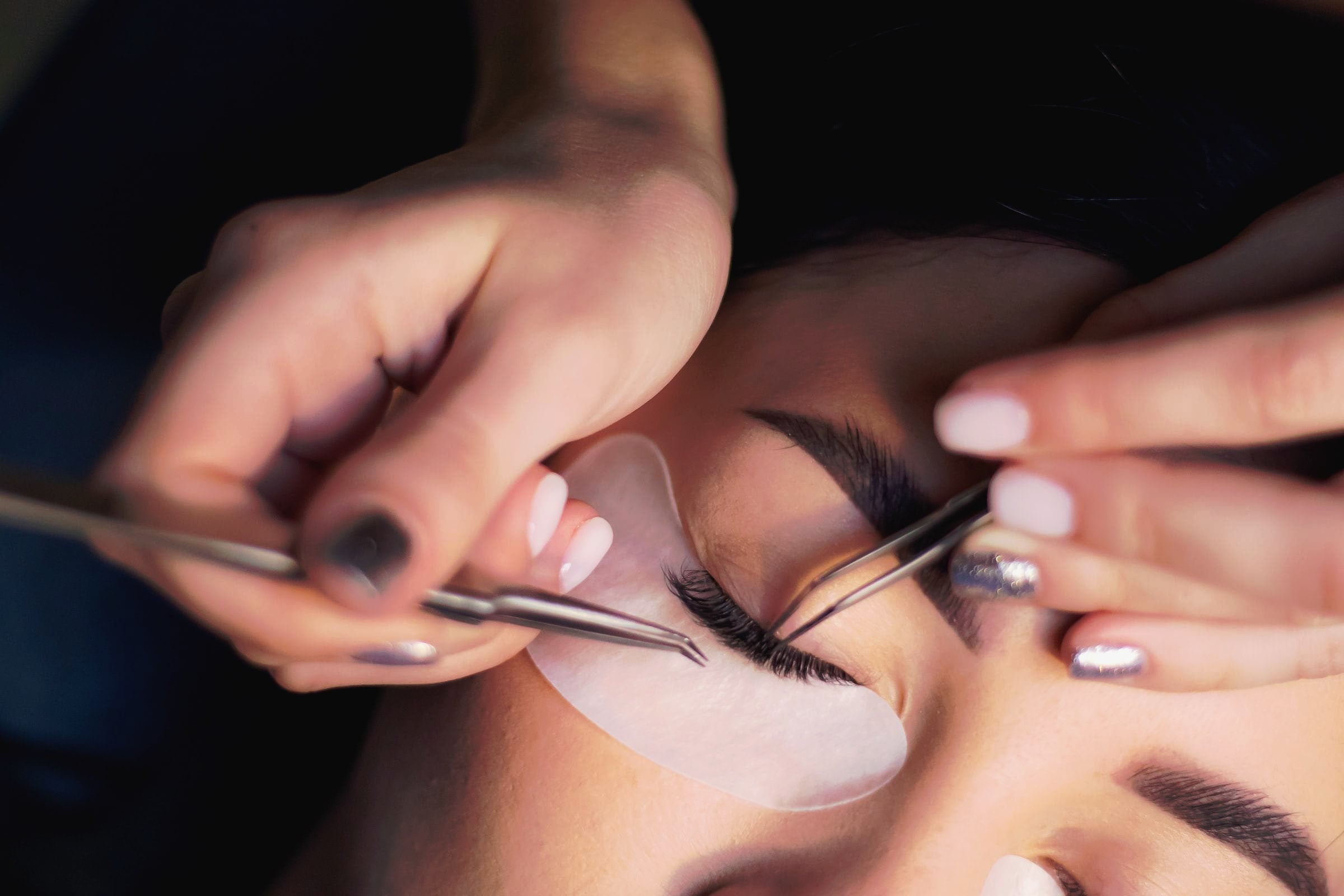 A lash technician applying eyelash extensions with fine tweezers.
