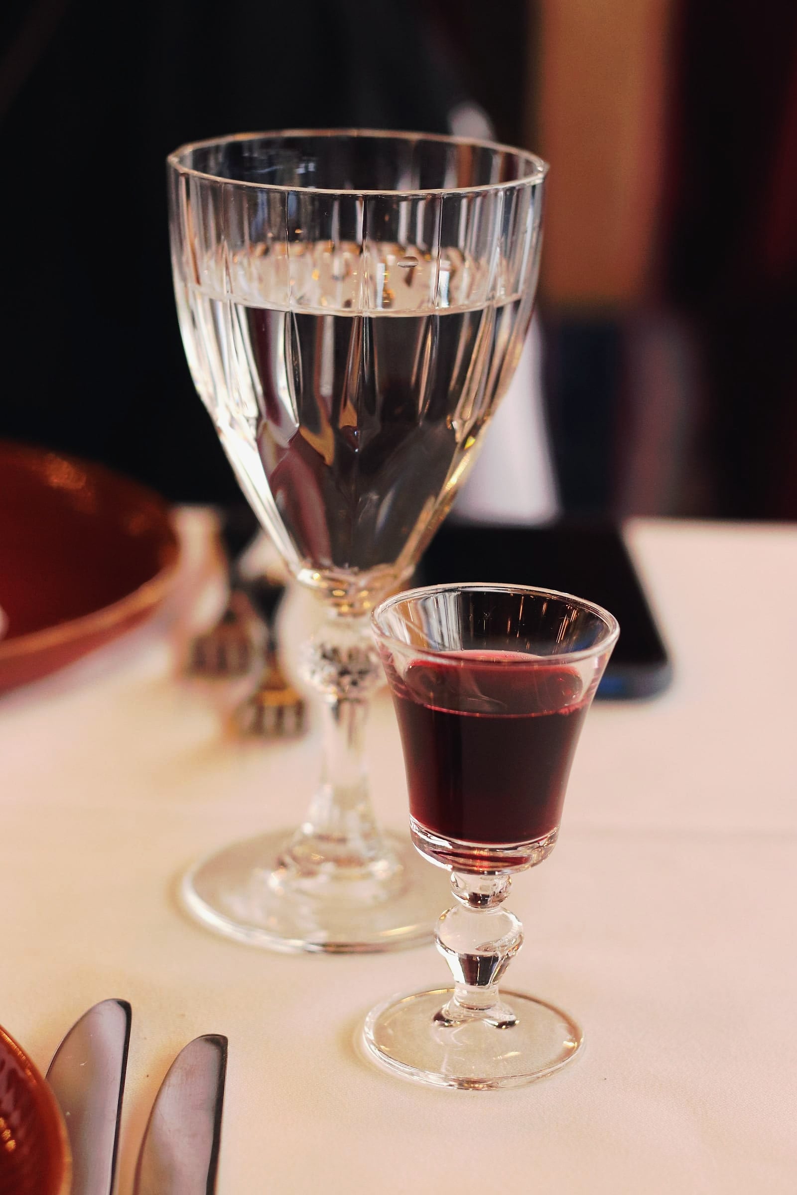 A small glass of deep red fortified wine on a white tablecloth.