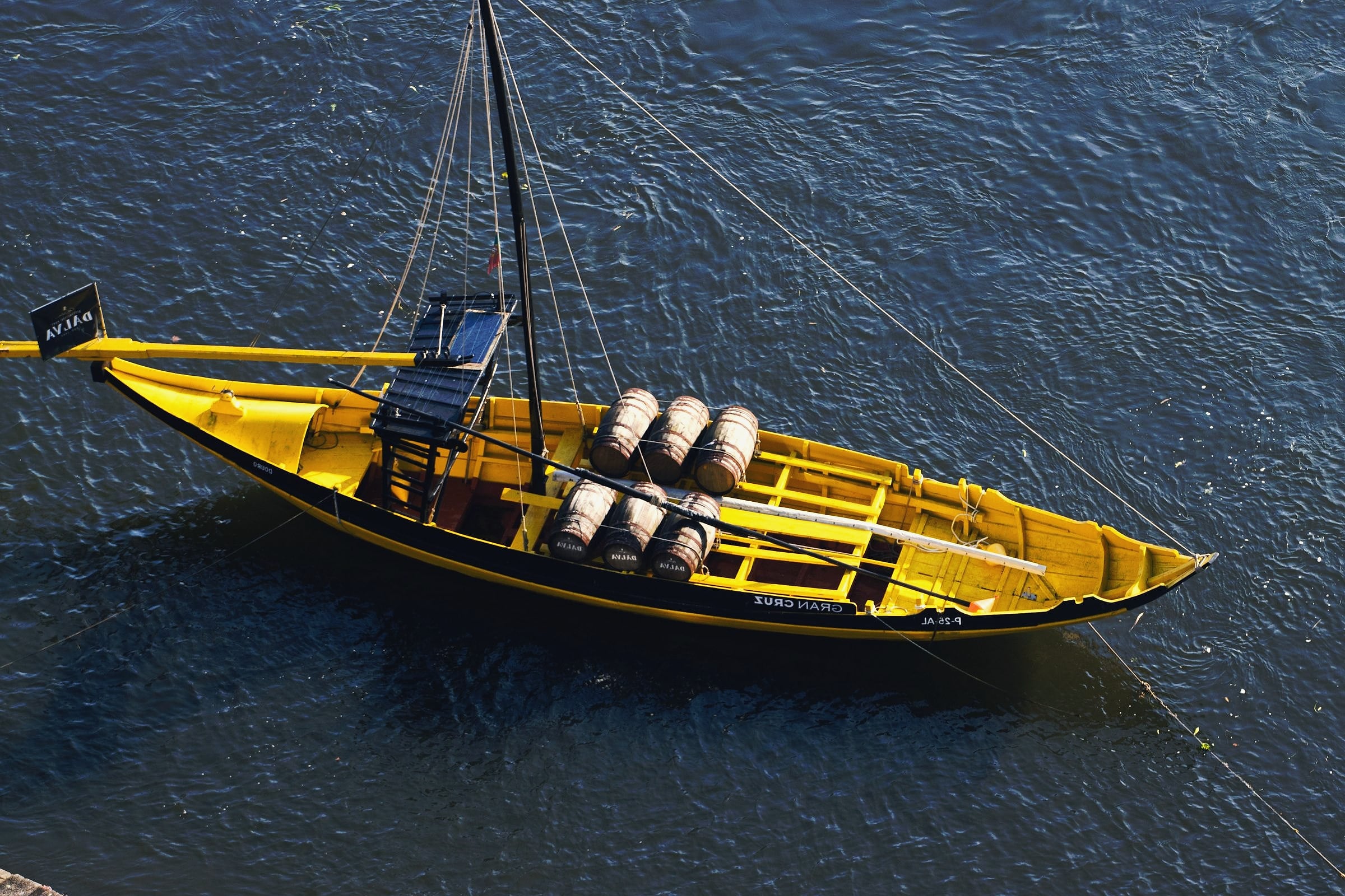 A yellow rabelo boat loaded with wine barrels on the Douro River in Porto, seen from above.
