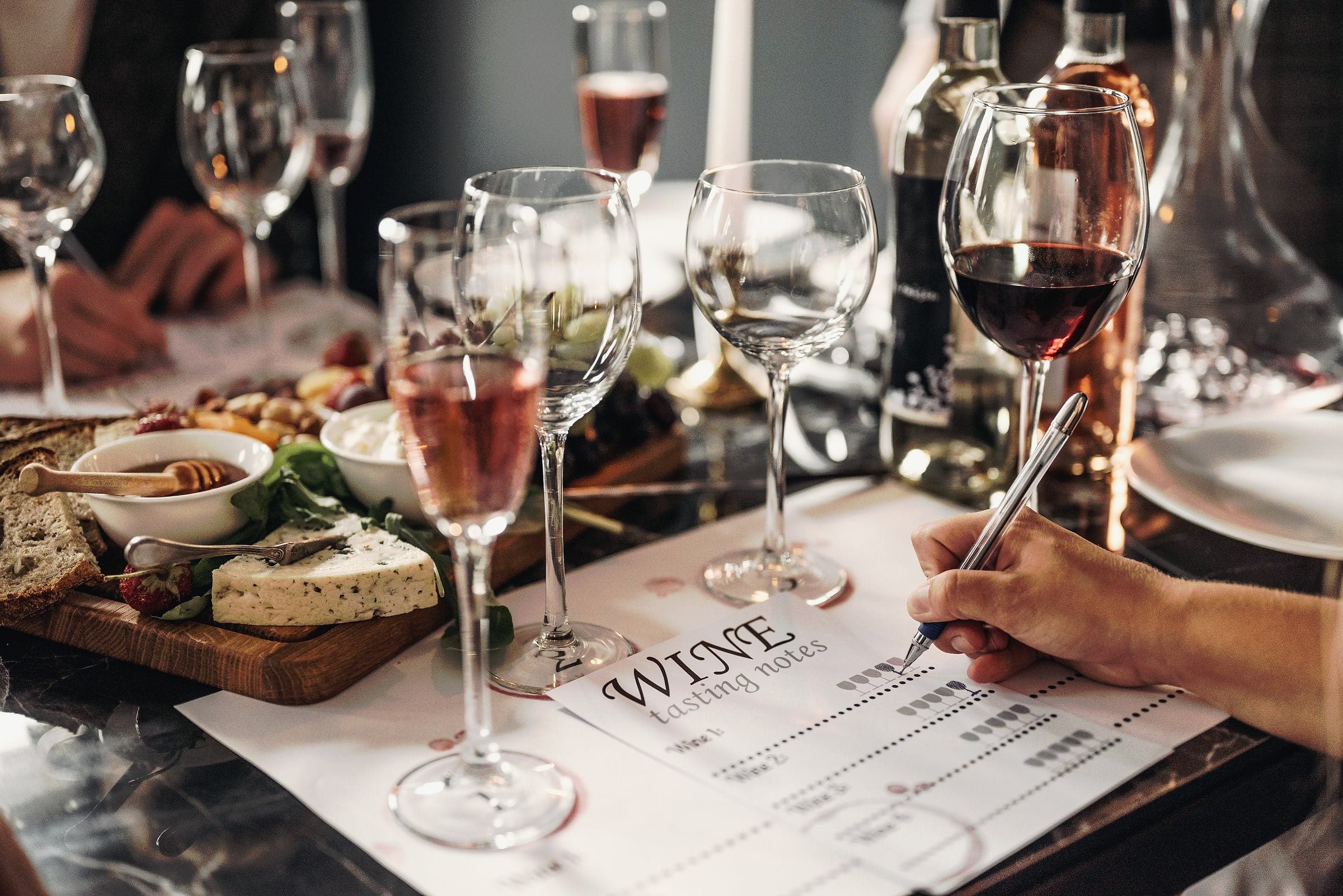 Glasses of red and rosé wine beside a cheese board and a tasting sheet.